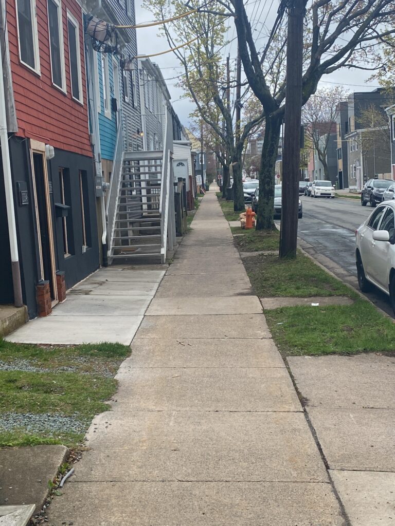 A long concrete sidewalk extends down the street with very few visual obstructions and good open space on either side.