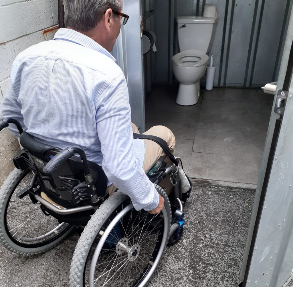 A wheelchair user enters an outdoor single-stall accessible washroom at Stillwell Beergarden.