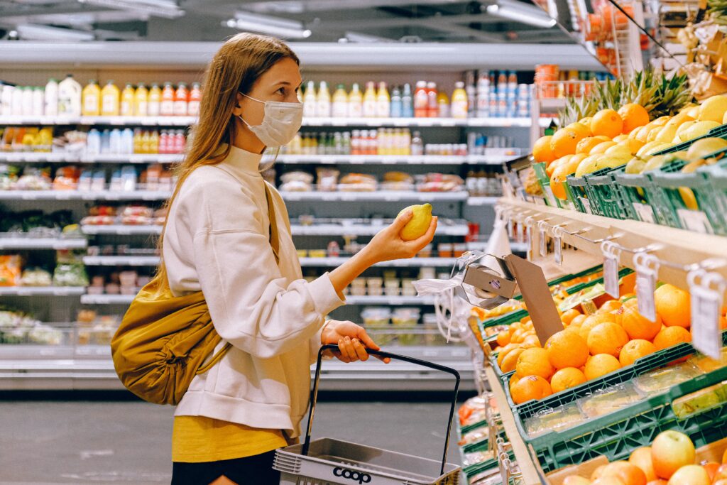 A woman wearing a face mask selects lemons from a supermarket fruit stand.