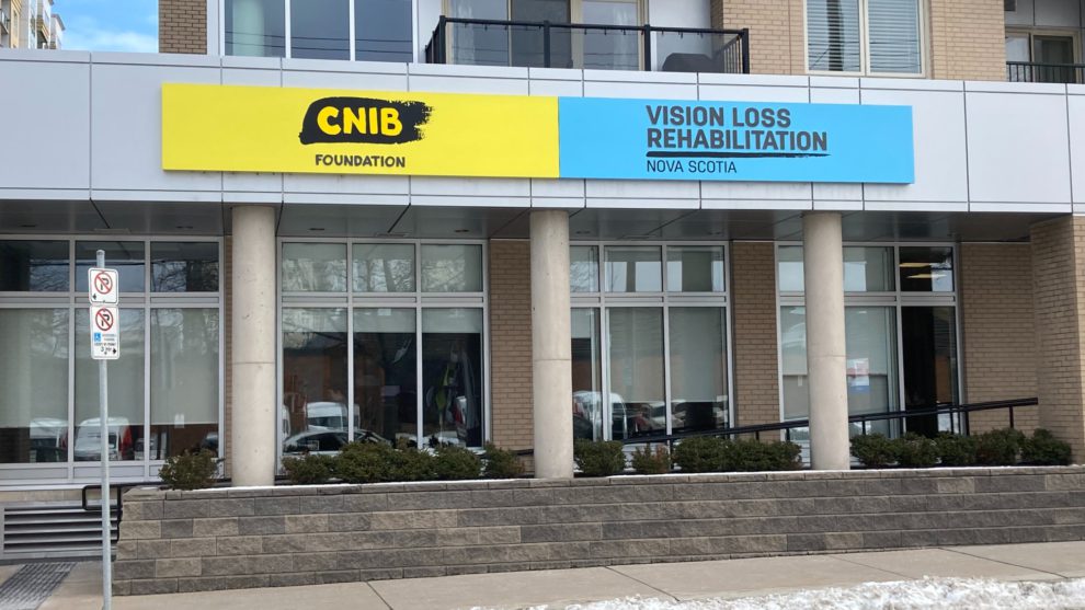A building facade with lots of windows and a bright yellow CNIB Foundation sign in front. 