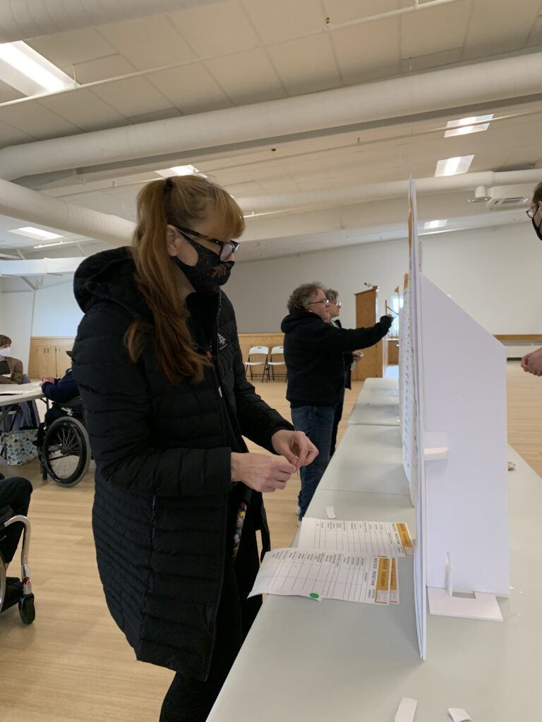 A woman wearing a mask standing in front of a poster.