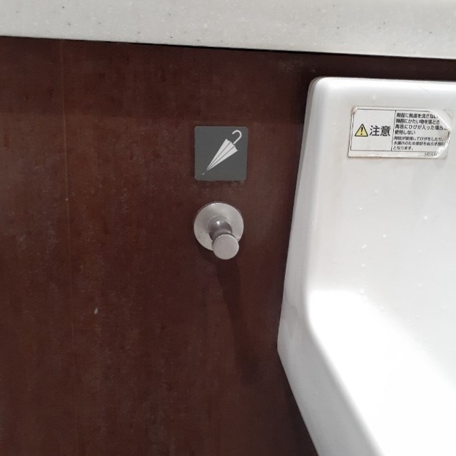 A silver knob with an umbrella icon above it on a wall.
