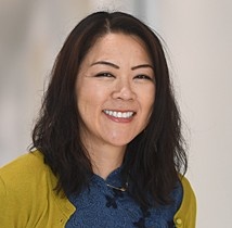 A smiling woman with dark hair wearing a yellow sweater