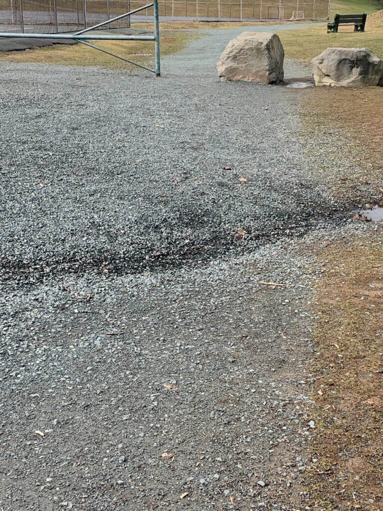 A gutter-like dip cuts across a gravel path in a park.