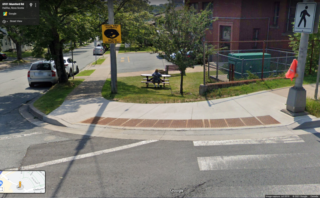 A street corner with a large curb cut with tactile attention indicators and painted crosswalks crossing both streets