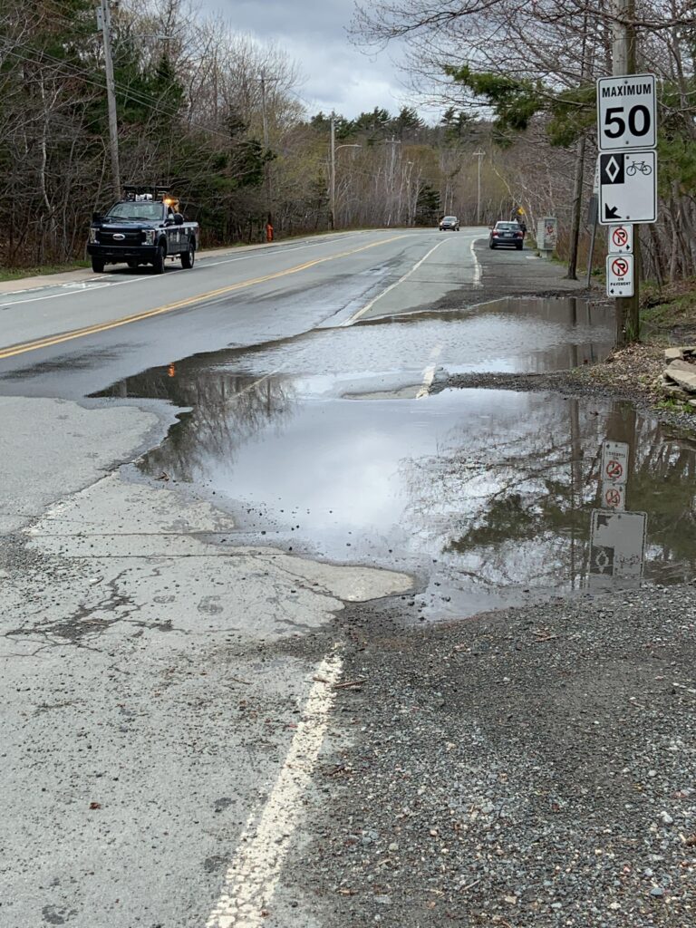 Gravel roadside and bike lane is flooded by a large puddle. 