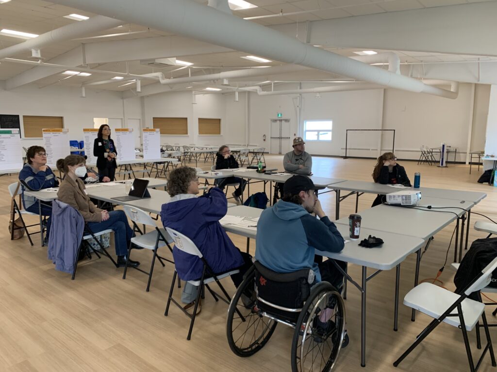 Several individuals, some using wheelchairs, sitting around a u-shaped table in a large room.