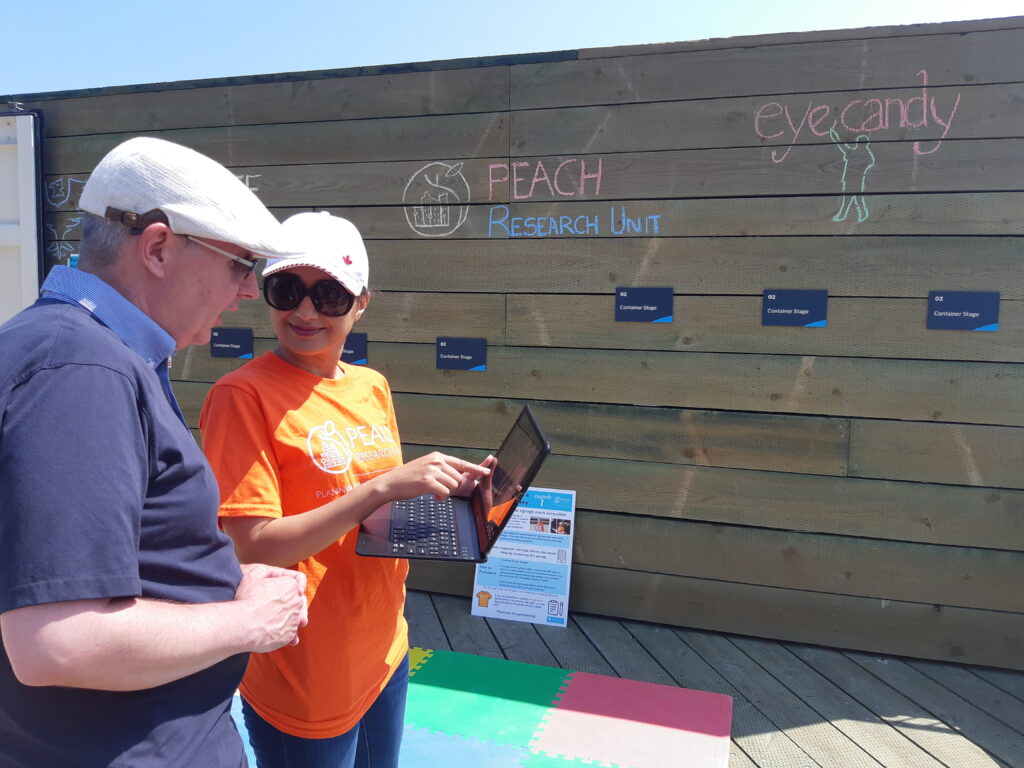 A woman wearing an orange t-shirt showing a tablet screen to a man standing next to her.