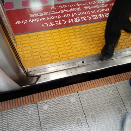 The threshold of an open subway car door with yellow tactile attention indicators on the floor and a small gap to a subway platform.
