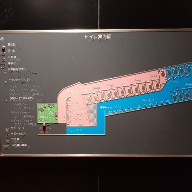 A tactile map on a black wall showing the floor plan of two multi-stall gendered washrooms. 
