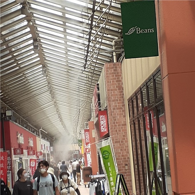 Ceiling sprinklers spraying mist down onto an indoor street full of pedestrians.