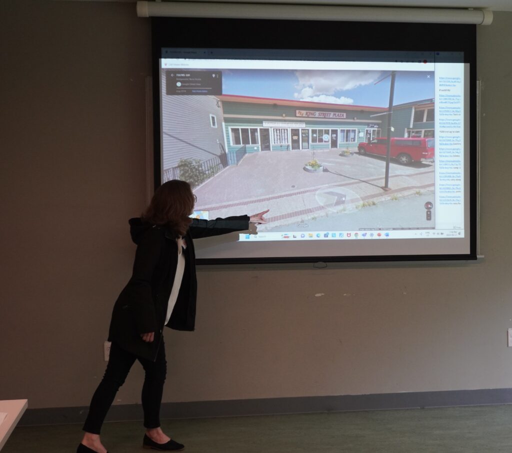 A woman pointing with her arm outstretched at a screen displaying a Google Maps streetview.