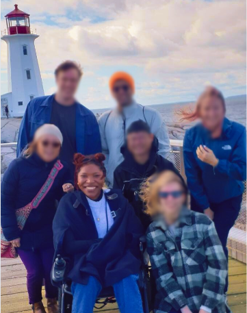 A woman on a wheelchair with friends around her on the viewing deck with lighthouse in the background.
