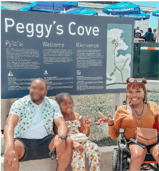 A woman on a wheelchair with family by a Welcome to Peggy's Cove sign.